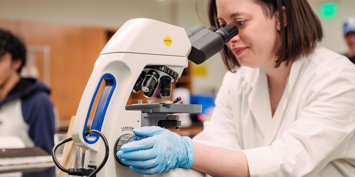 Histotech instructor looking at a slide through a microscope.
