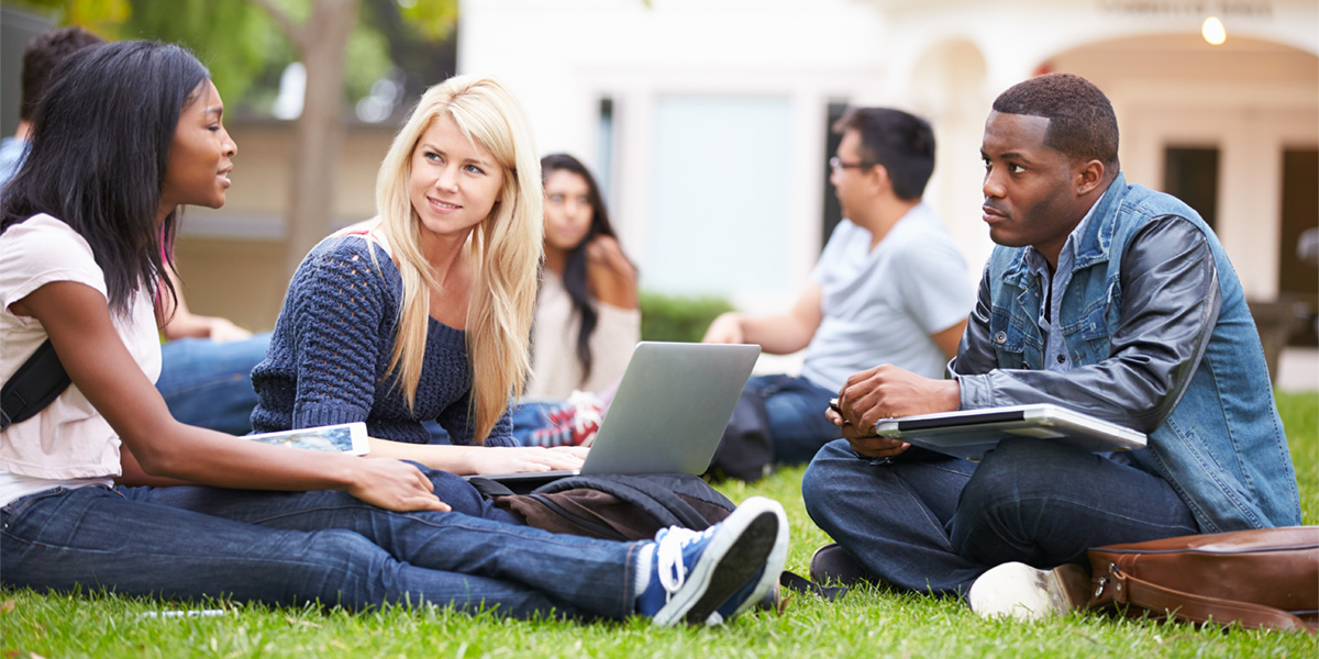 Students talk while sitting on college lawn.